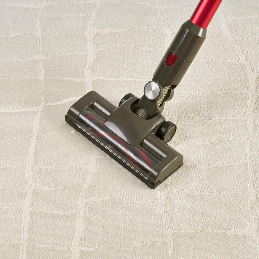 An ivory luxury Wilton jacquard area rug is shown being vacuumed, highlighting its raised grid texture, plush dimensional surface, and premium easy-care finish for refined living rooms and elegant bedrooms.