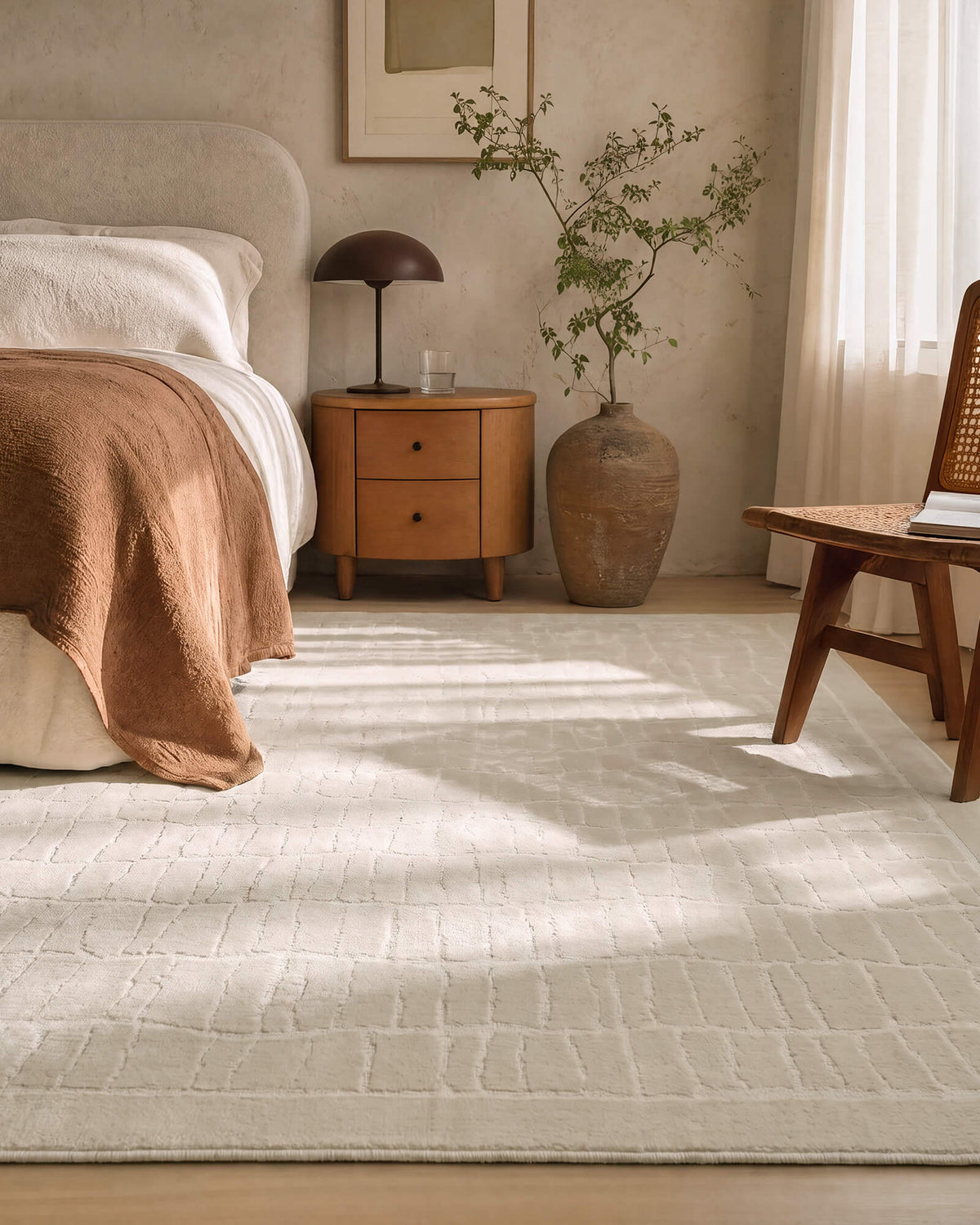 An ivory luxury Wilton jacquard area rug with a raised grid texture adds sculptural softness to an elegant bedroom with warm wood furniture, layered bedding, natural sunlight, and refined neutral decor.