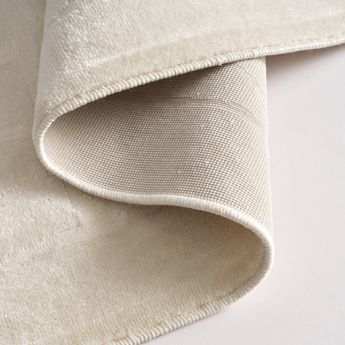 A close-up view of an ivory luxury Wilton jacquard rug showing its folded corner, plush abstract block texture, woven backing, and refined bound edge for premium living room and bedroom styling.