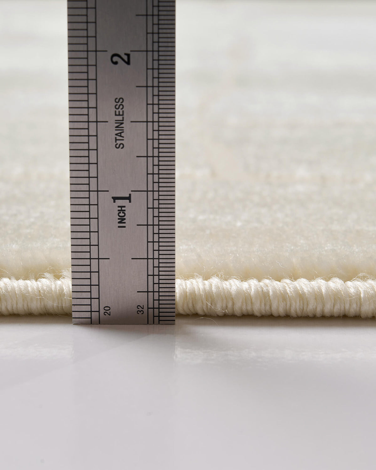 A close-up view of an ivory luxury Wilton jacquard rug showing its ruler-measured pile height, plush abstract block texture, and refined bound edge for elevated living room and bedroom decor.