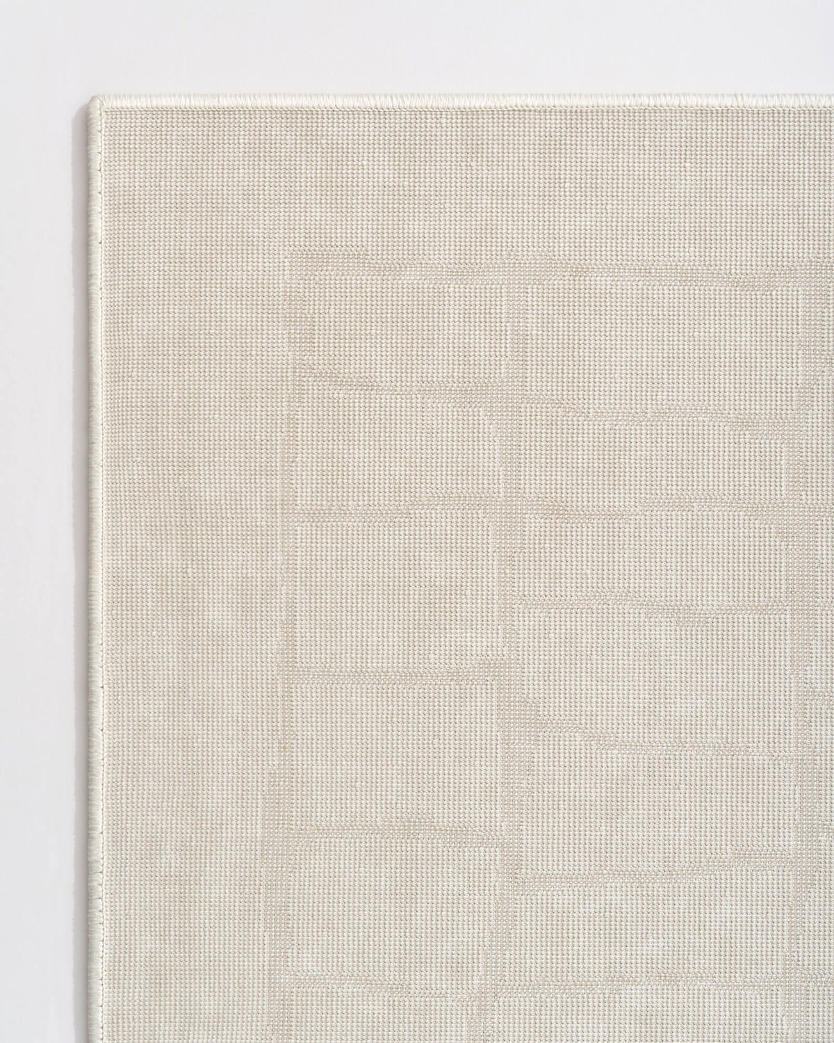 A close-up reverse corner view of an ivory luxury Wilton jacquard rug highlights its structured woven backing, tonal raised block pattern, and refined bound edge for elevated living room and bedroom styling.
