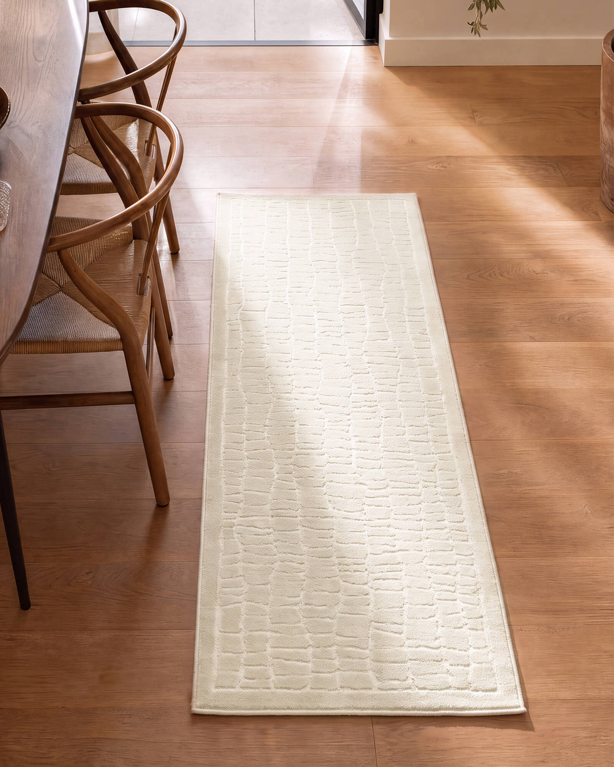 An ivory luxury Wilton jacquard runner rug with a raised crackle grid texture adds refined softness to a sunlit kitchen hallway with warm wood flooring, woven chairs, and elevated neutral decor.