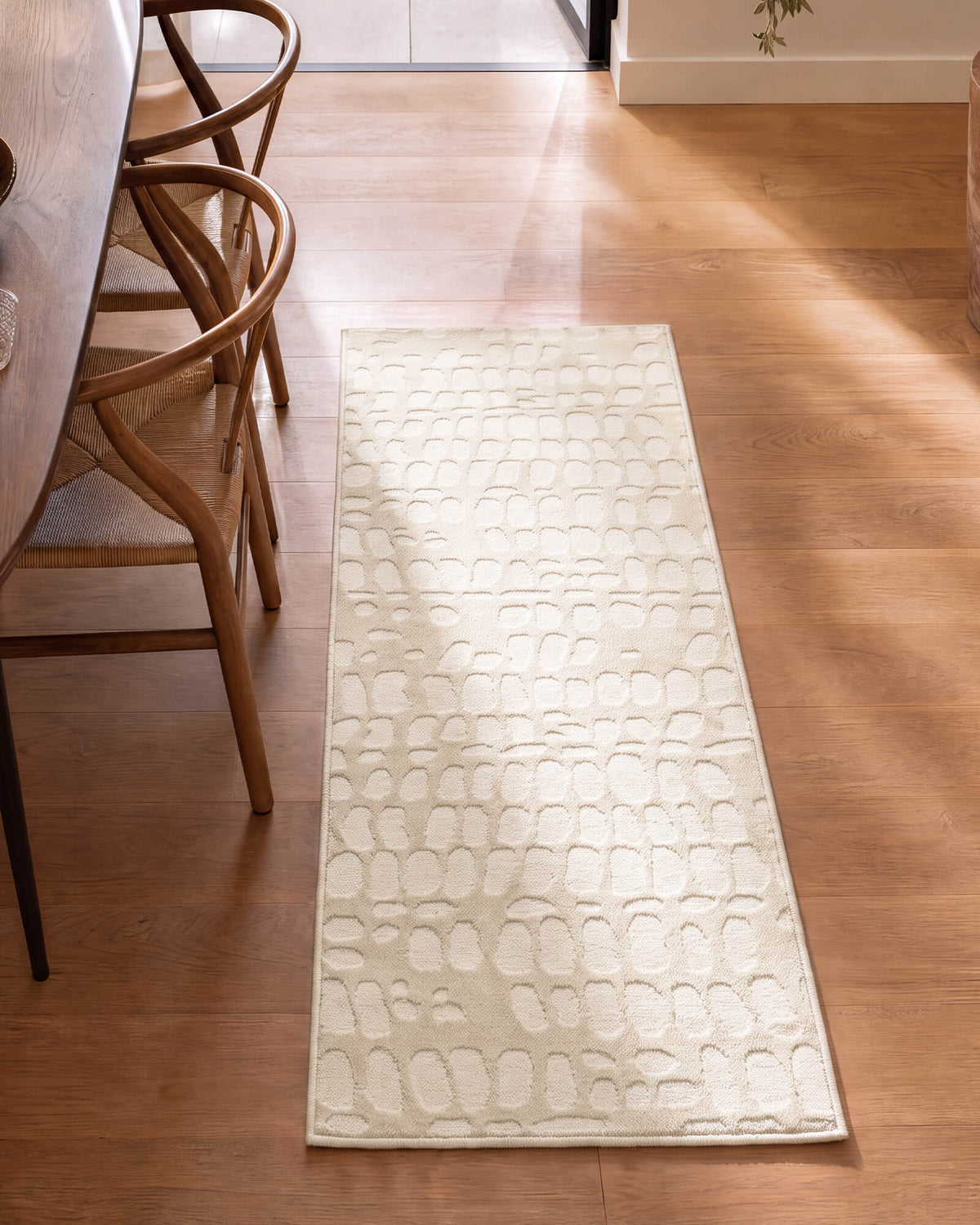 An ivory luxury Wilton jacquard runner rug with a raised pebble-inspired pattern adds sculptural softness to a sunlit kitchen hallway with warm wood floors, woven chairs, and refined neutral decor.