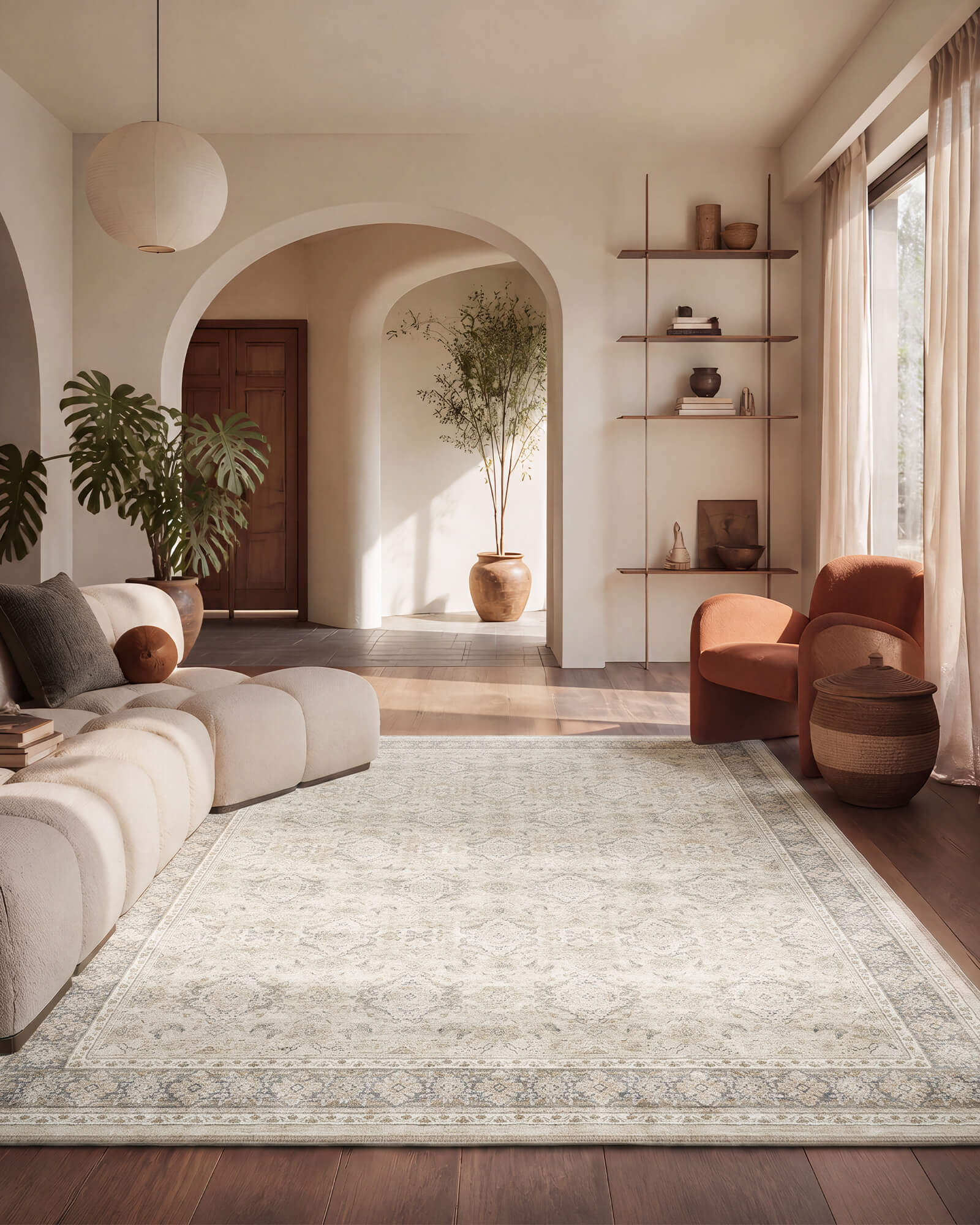 An ivory neutral vintage washable area rug with a soft distressed border pattern adds calm texture to an arched living room with a modular sofa, rust accent chair, open shelving, and warm natural light.