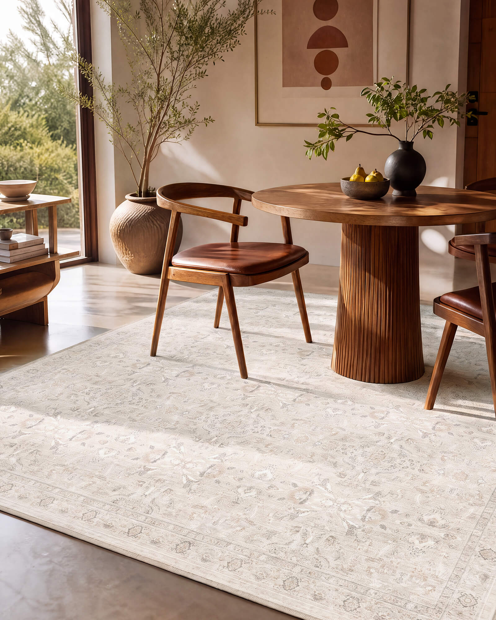 An ivory neutral vintage washable rug with a soft faded medallion pattern adds understated elegance to a warm dining area with a round pedestal table, leather chairs, natural wood tones, and sunlit modern decor.
