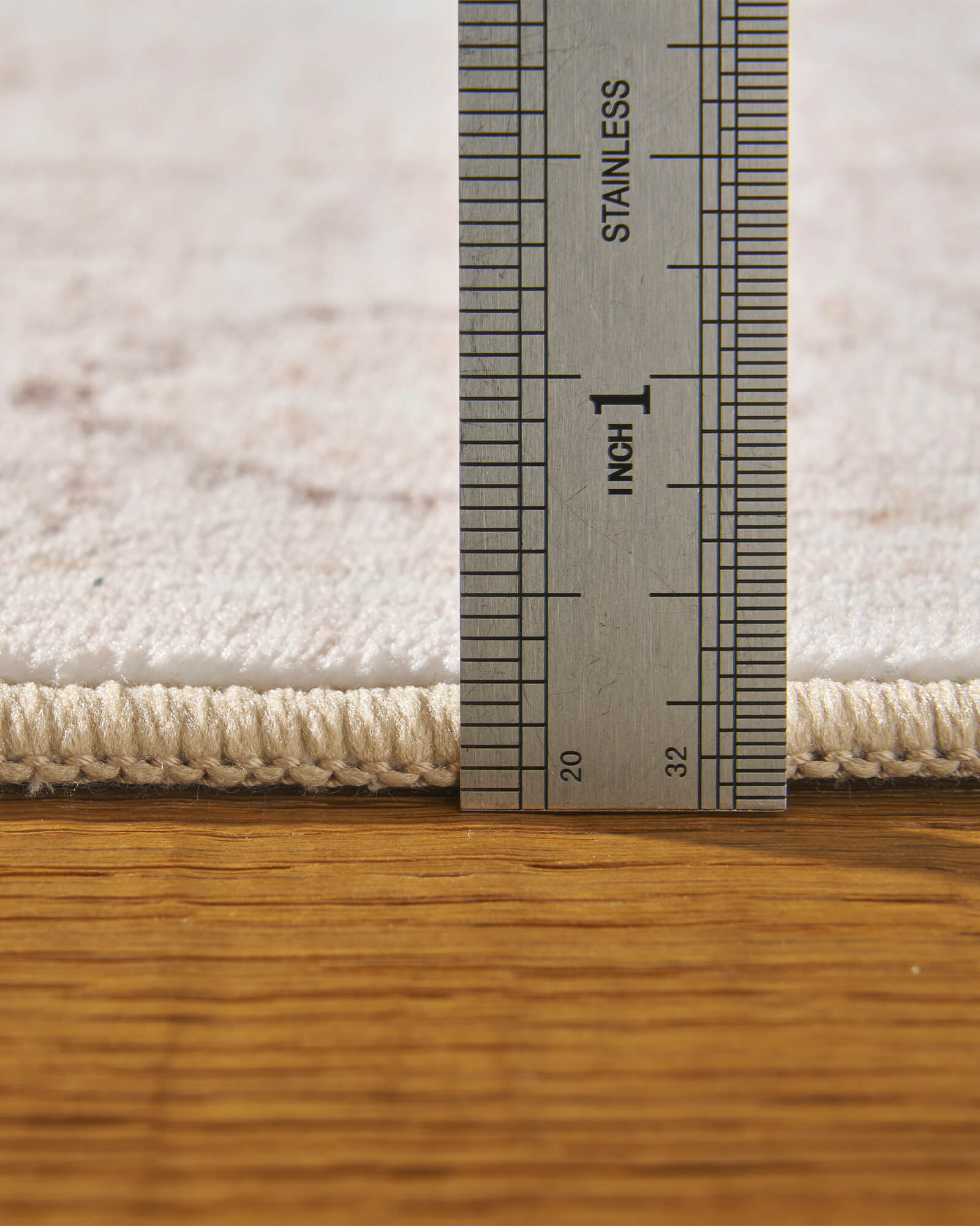 A close-up view of an ivory neutral vintage washable rug showing its ruler-measured pile height, soft low-profile surface, and bound edge for easy placement in living rooms, bedrooms, and family spaces.