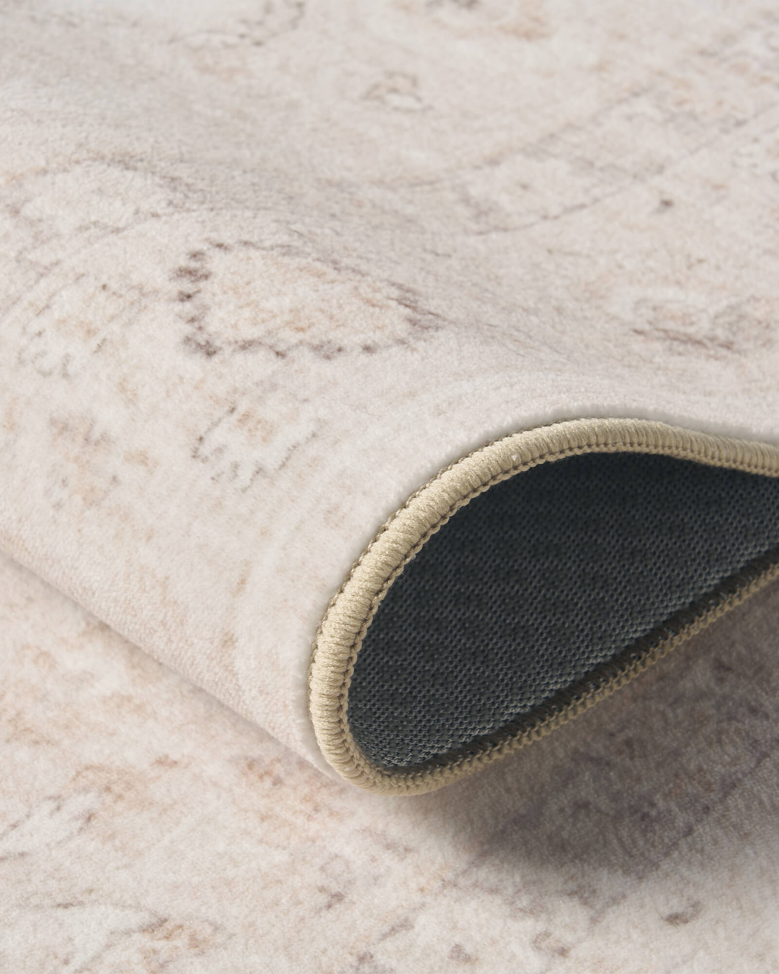 A close-up view of an ivory neutral vintage washable rug showing its rolled corner, dark backing, bound edge, and soft distressed surface for flexible everyday use in living rooms, bedrooms, and cozy home spaces.