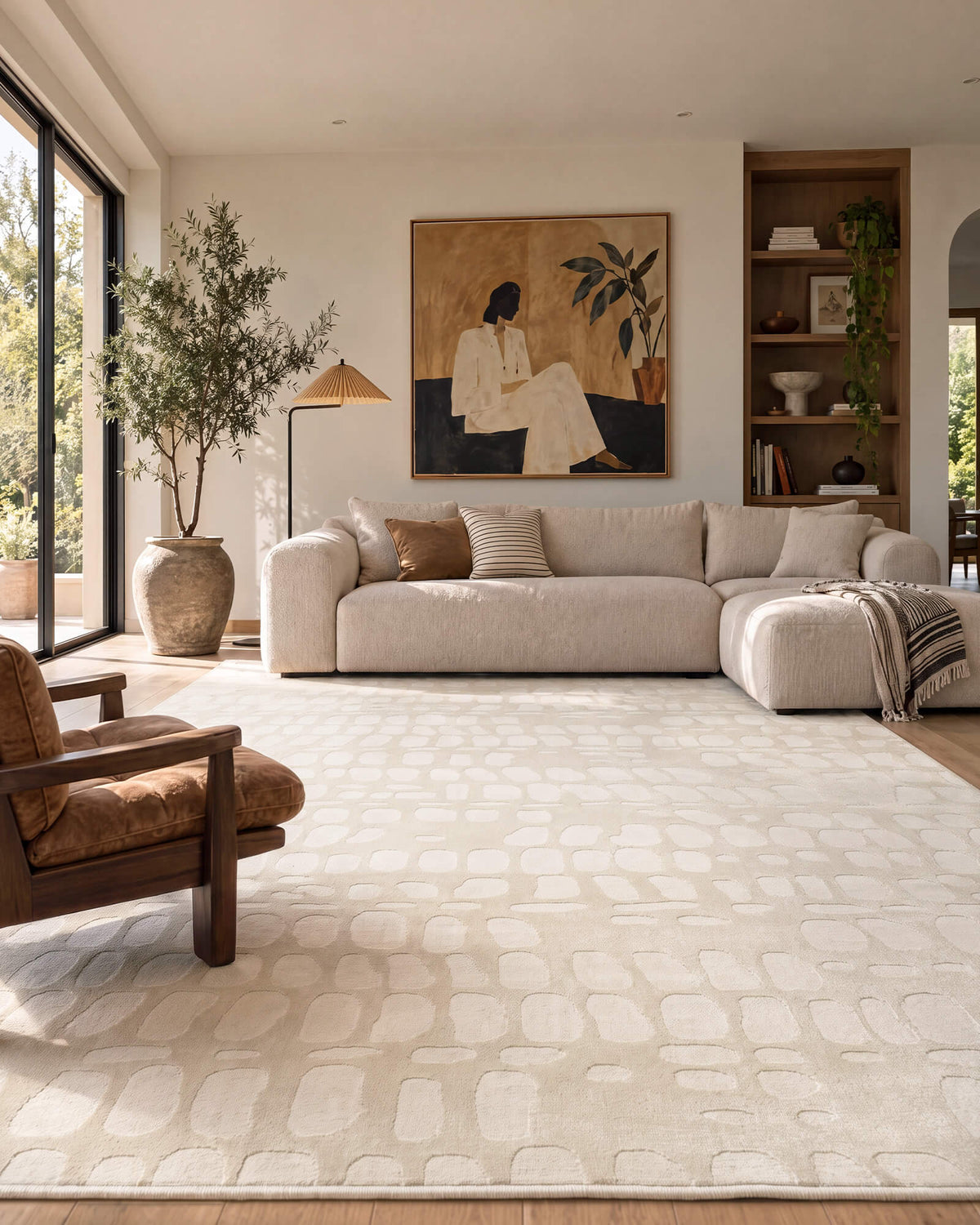 An ivory premium Wilton jacquard area rug with raised pebble-inspired texture adds sculptural softness and refined dimension to a luxury living room with a sectional sofa, curated artwork, warm wood accents, and natural light.
