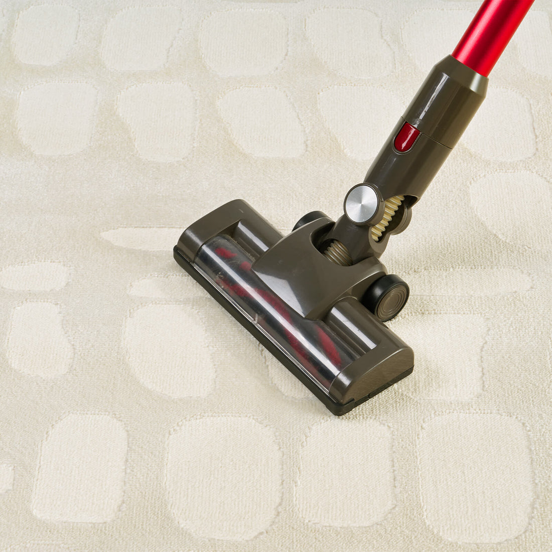 An ivory premium Wilton jacquard area rug is shown being vacuumed, highlighting its raised pebble-inspired pattern, plush dimensional texture, and refined easy-care surface for elevated living room and bedroom styling.