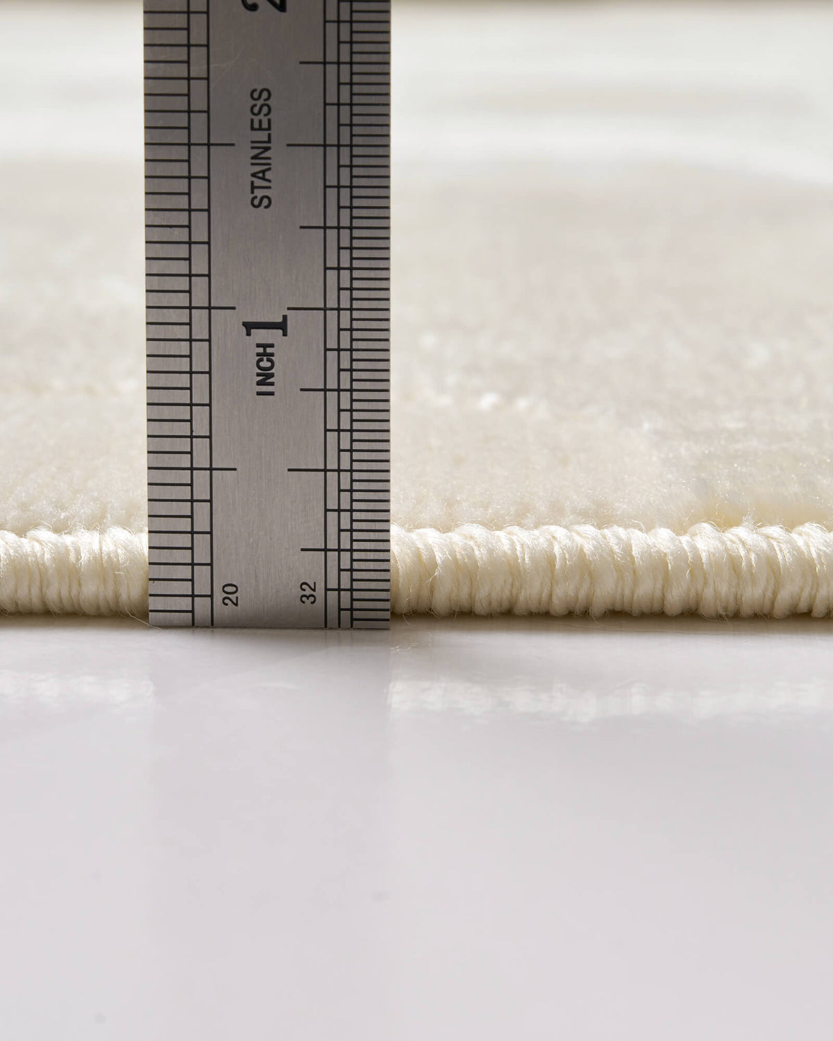 A close-up view of an ivory premium Wilton jacquard rug showing its ruler-measured pile height, plush raised texture, and refined bound edge for elevated living room and bedroom styling.