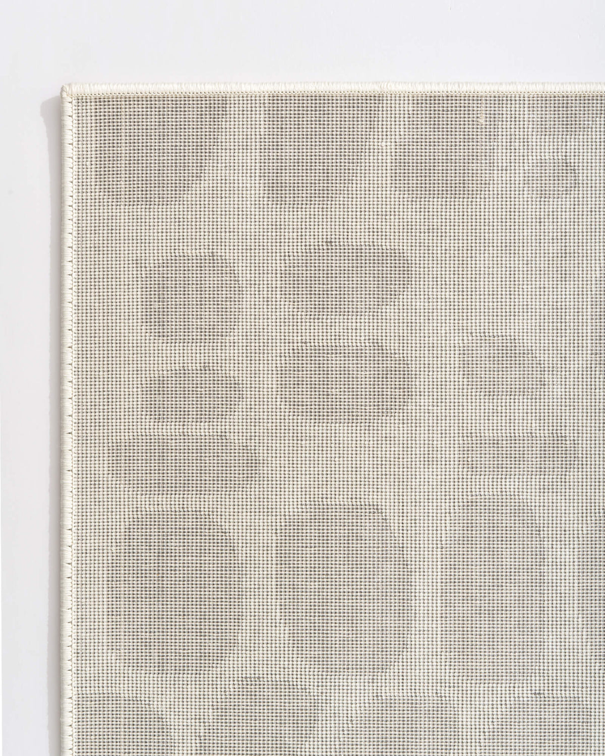 A close-up reverse corner view of an ivory premium Wilton jacquard rug highlights its structured woven backing, tonal pebble-inspired pattern, and refined bound edge for elevated living room and bedroom styling.