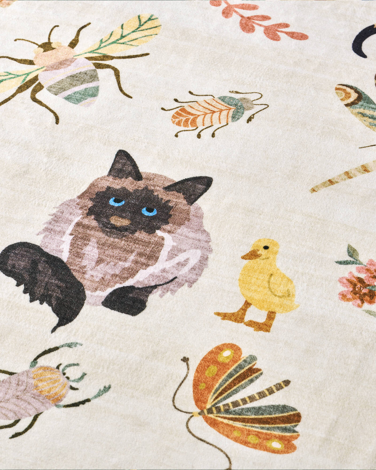 A close-up view of an ivory soft kids rug highlights its cute cat, duck, butterfly, and bug illustrations, offering a gentle comfortable surface and playful charm for nurseries, playrooms, and children’s bedrooms.