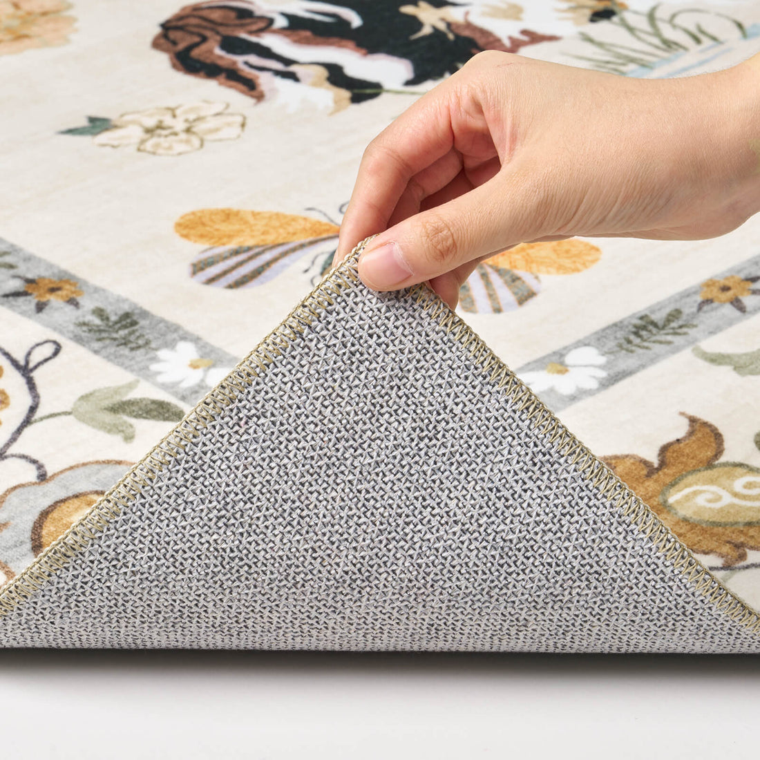 A close-up view of an ivory soft kids rug showing its folded corner, gray non-slip backing, cute animal border pattern, and neatly finished edge for safe, cozy nursery, playroom, and children’s bedroom use.