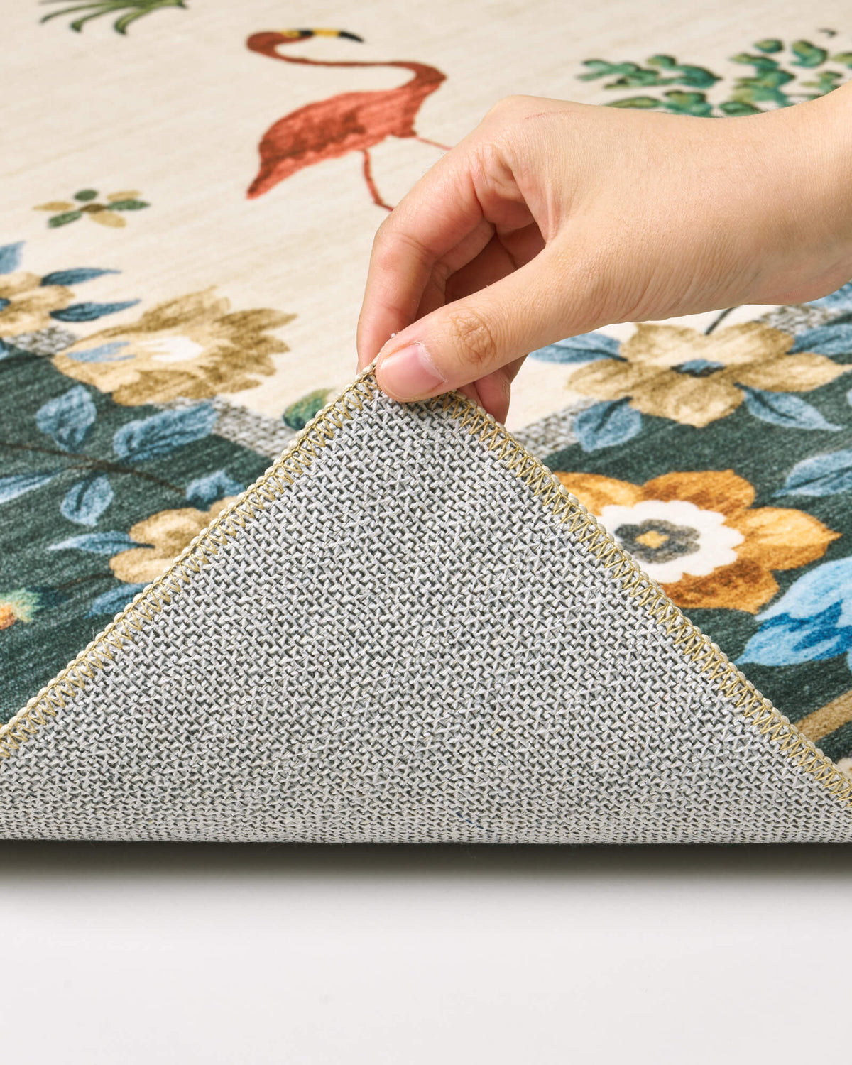 A close-up view of an ivory soft kids rug showing its folded corner, gray non-slip backing, green floral border, and neatly finished edge for safe, cozy nursery, playroom, and children’s bedroom use.
