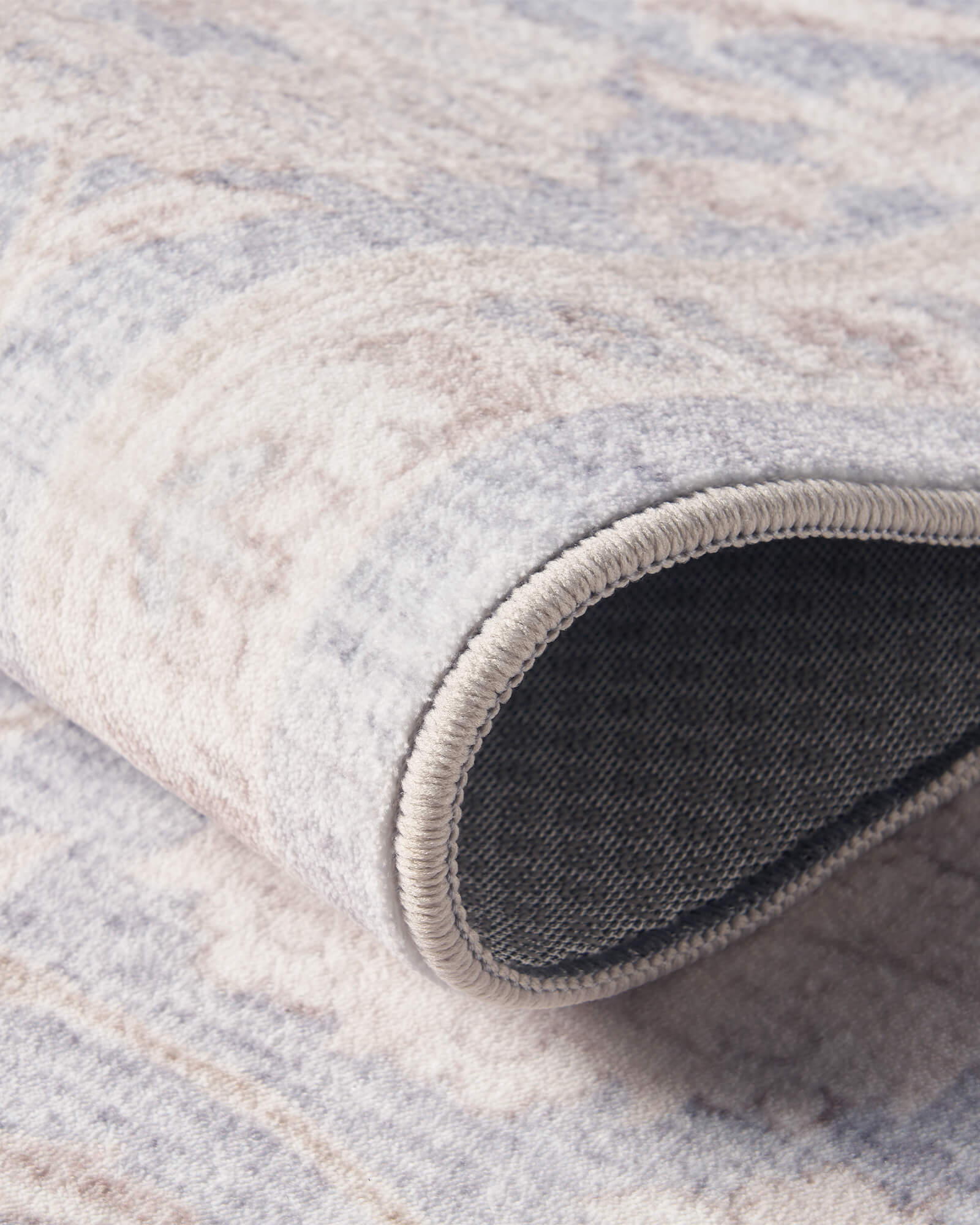 A close-up view of a light blue vintage washable rug showing its curled edge, dark backing, soft ornamental surface, and flexible low-pile construction for everyday living room and bedroom use.
