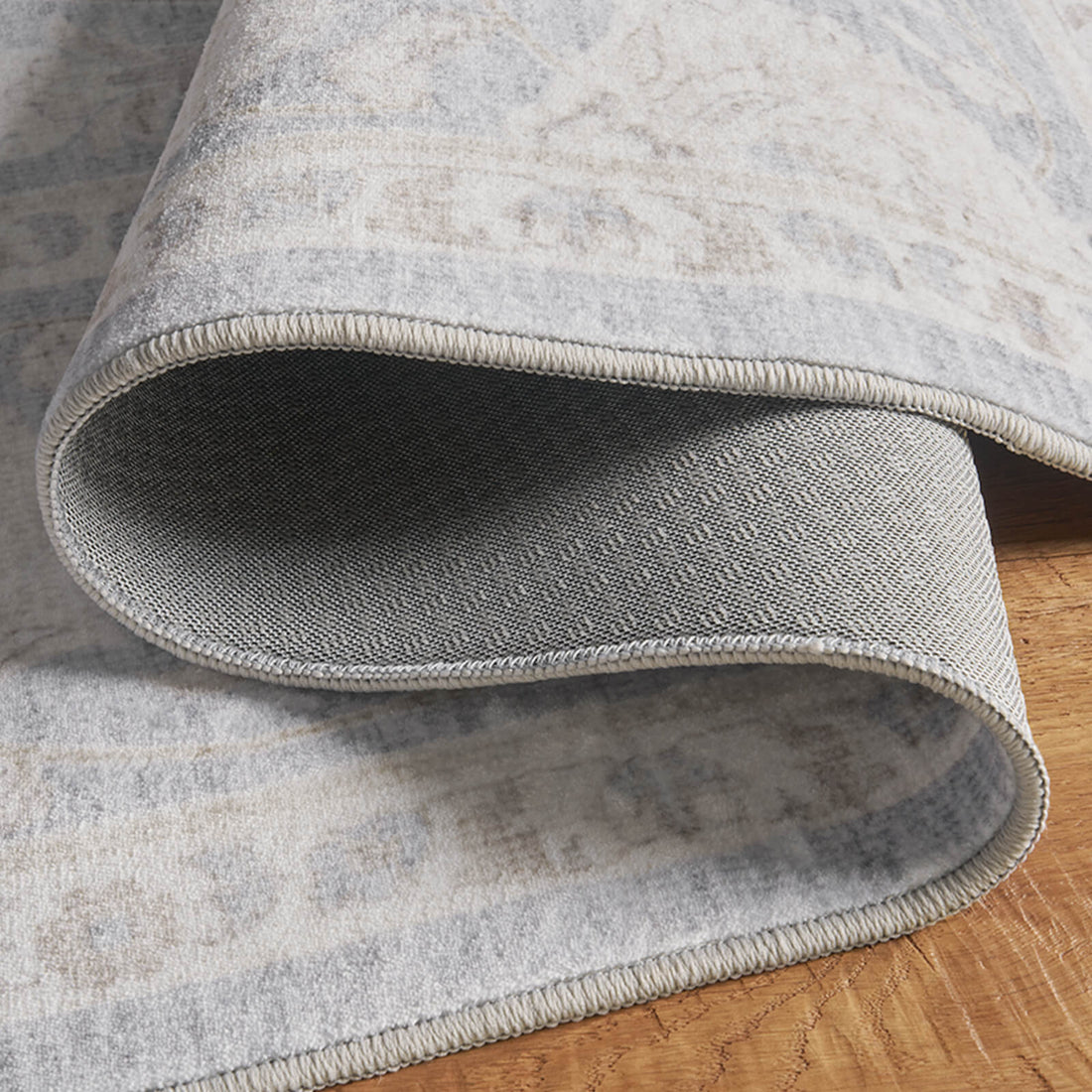 A close-up view of a light blue vintage washable rug showing its folded corner, gray backing, stitched edge, and flexible low-pile construction for easy everyday use in bedrooms, living rooms, and family spaces.