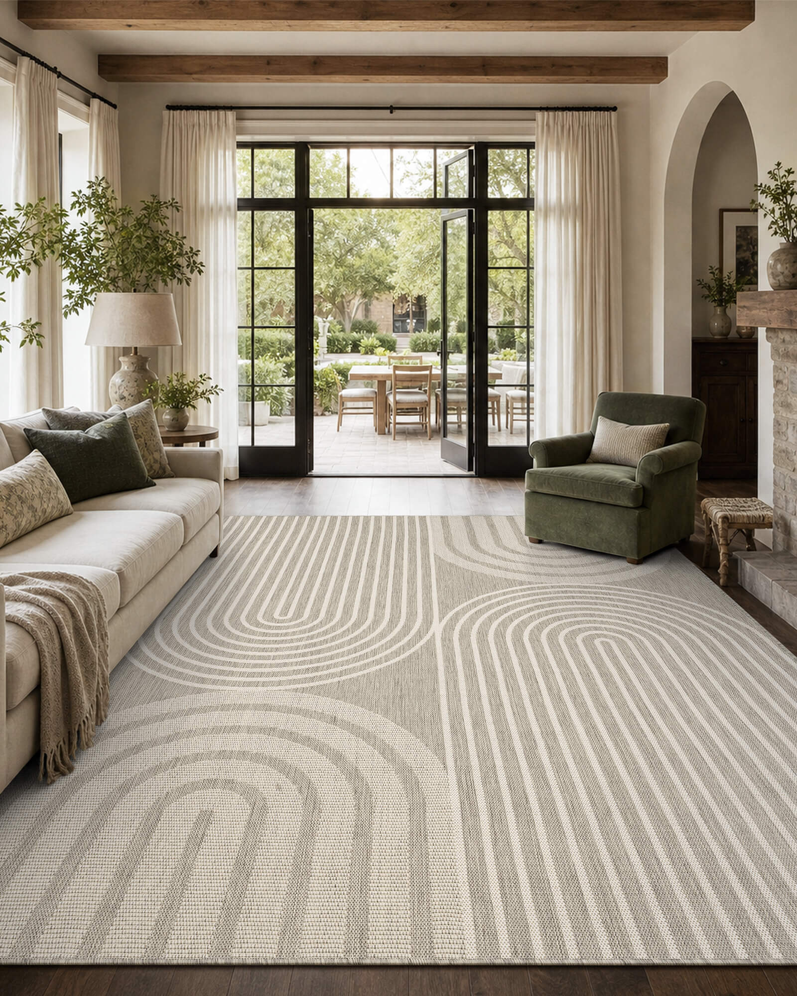 A light gray abstract indoor outdoor area rug with a modern arch line pattern adds soft texture to a French door living room with a cream sofa, green accent chair, wood beams, and relaxed modern farmhouse decor.