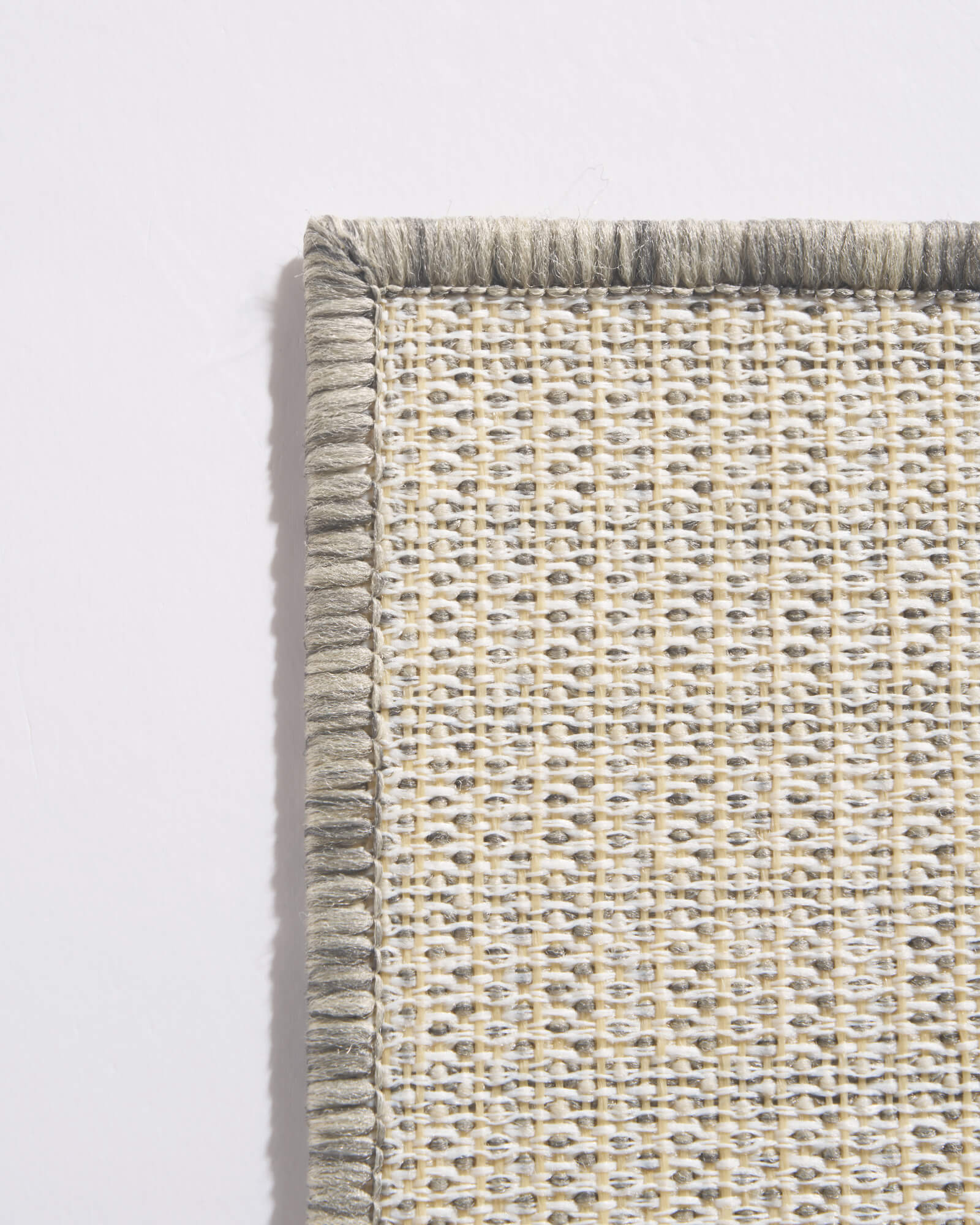 A close-up back view of a light gray abstract outdoor rug showing its woven grid backing, reinforced corner border, and durable construction for weather-resistant patio, deck, and porch use.