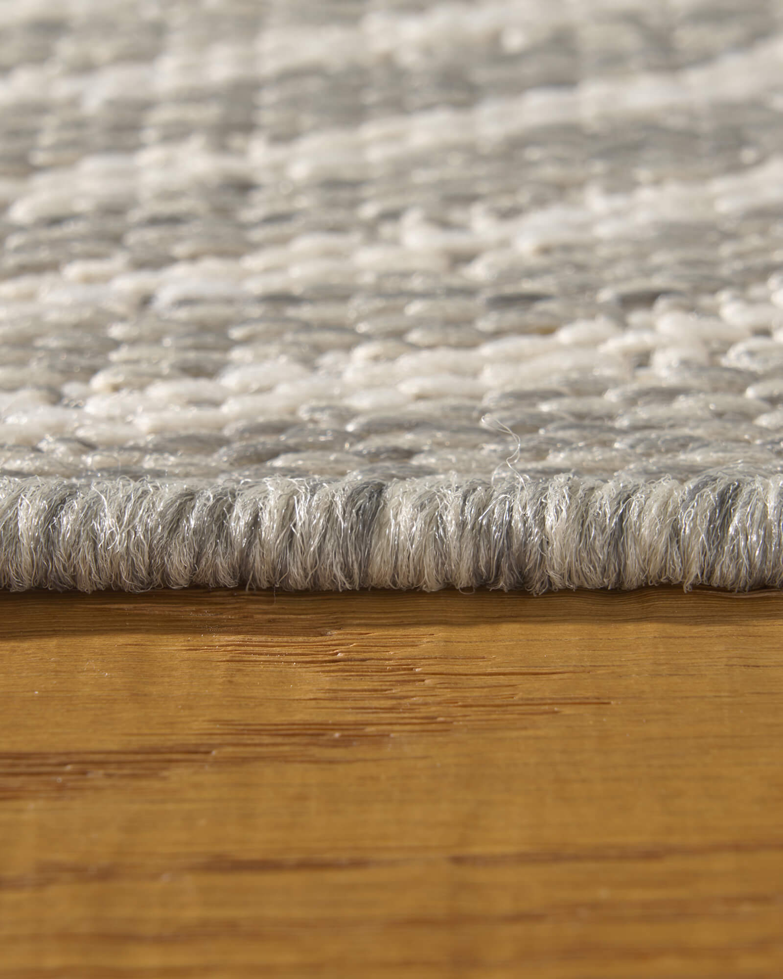 A close-up view of a light gray abstract outdoor rug showing its low-profile edge, woven raised line texture, and durable construction for patios, decks, porches, and outdoor living spaces.