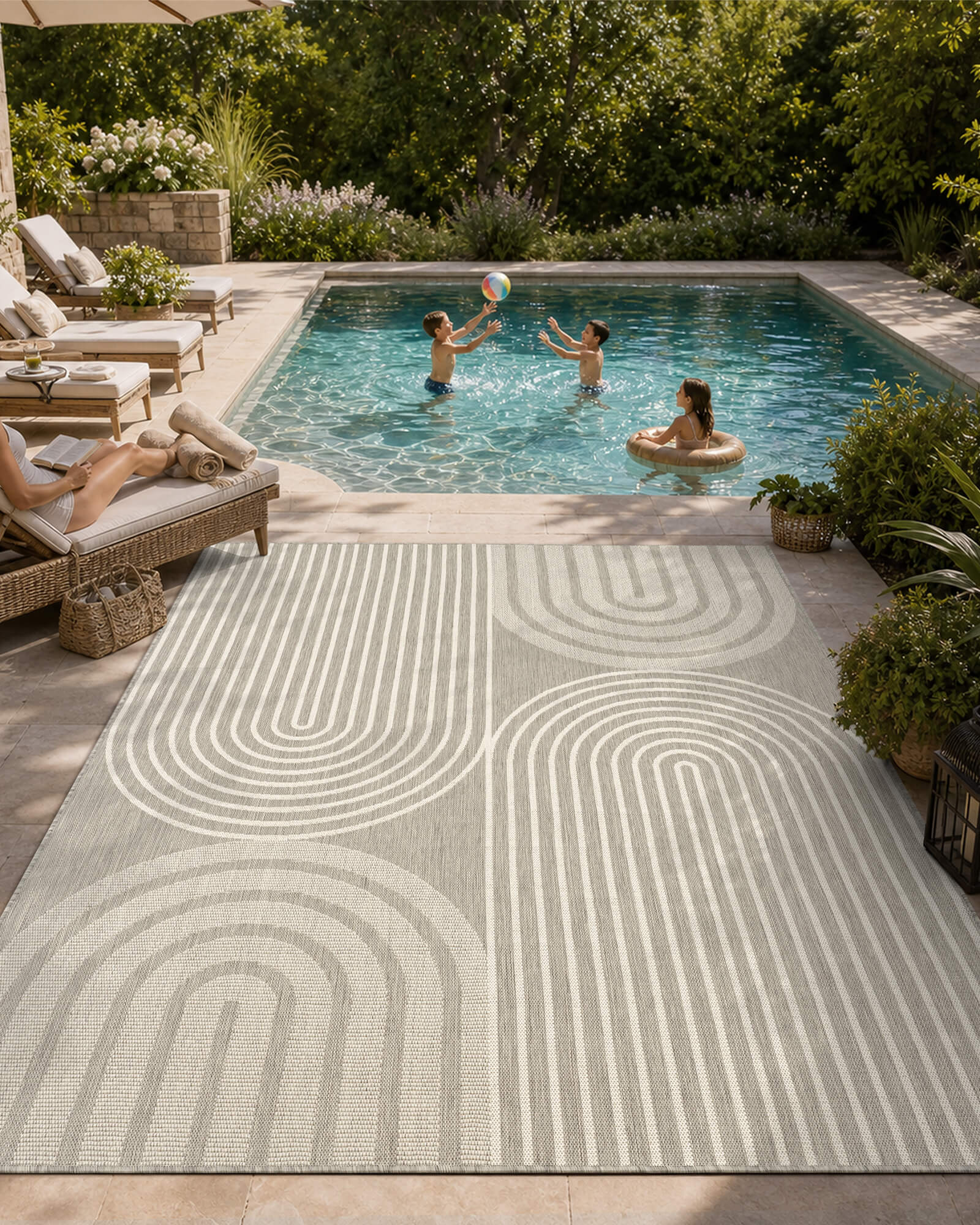 A light gray abstract outdoor rug with a modern arch line pattern creates a stylish poolside patio space with lounge seating, greenery, and family-friendly outdoor summer decor.