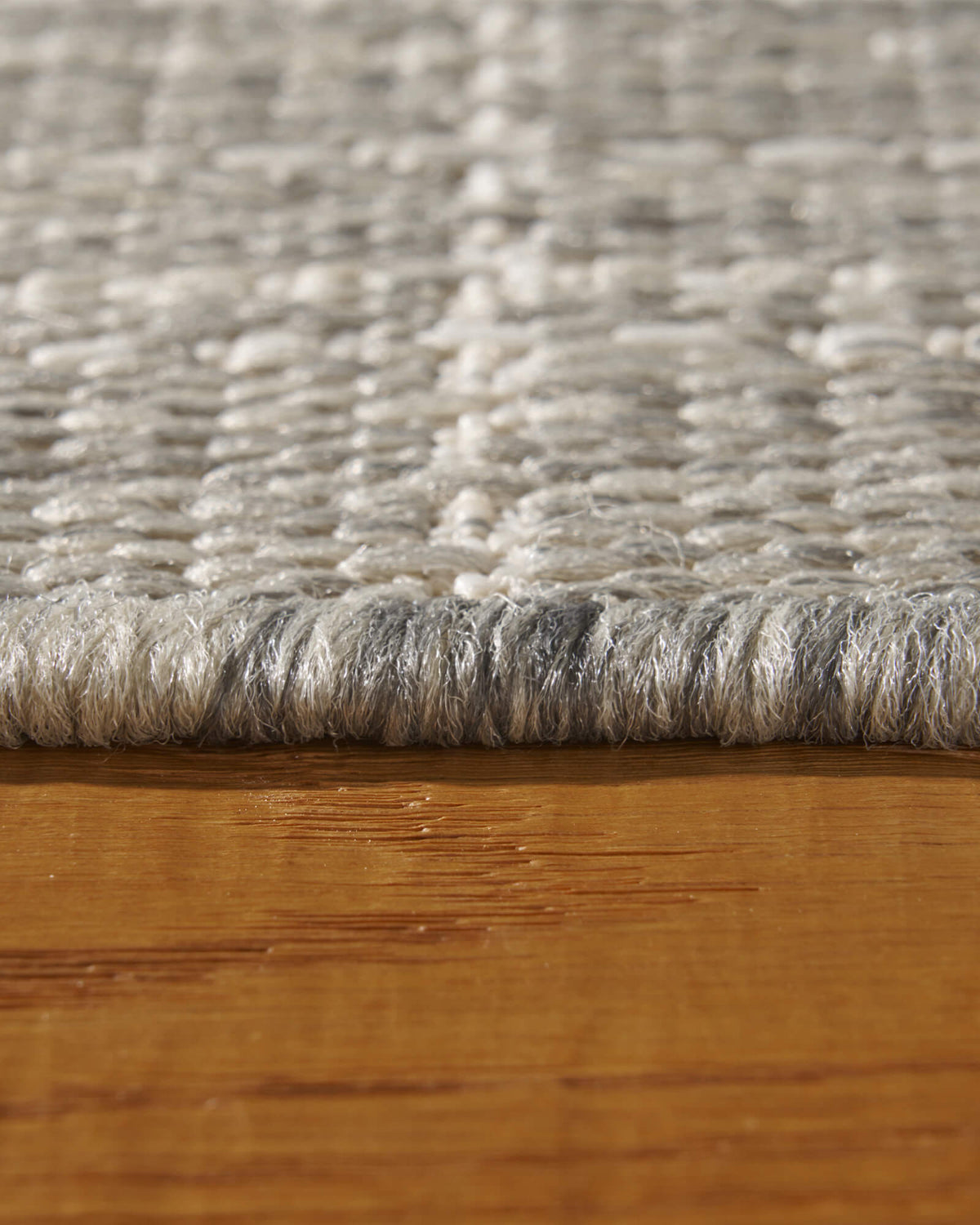 A macro close-up of a light gray grid outdoor rug shows its raised woven texture, low edge profile, and durable construction for patios, decks, porches, and outdoor living spaces.