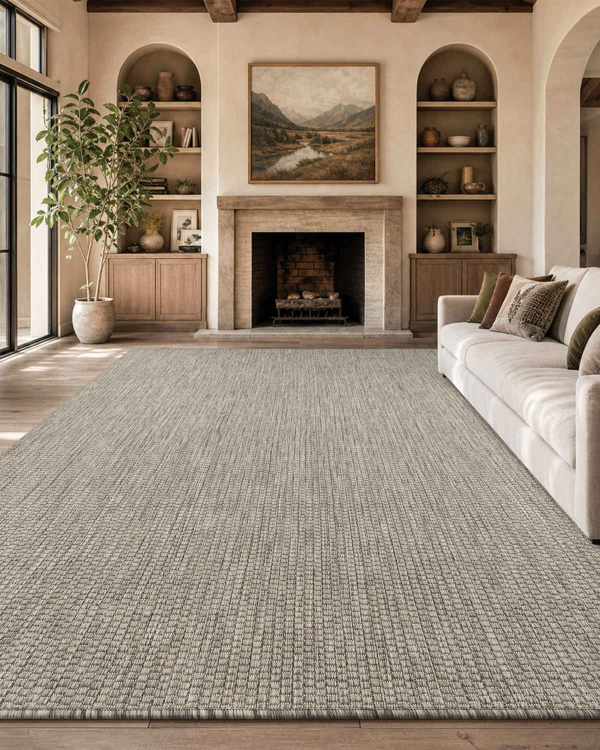 A light gray plain weave indoor outdoor area rug adds clean natural texture to a cozy fireplace living room with a cream sofa, built-in shelves, wood beams, and warm farmhouse decor.