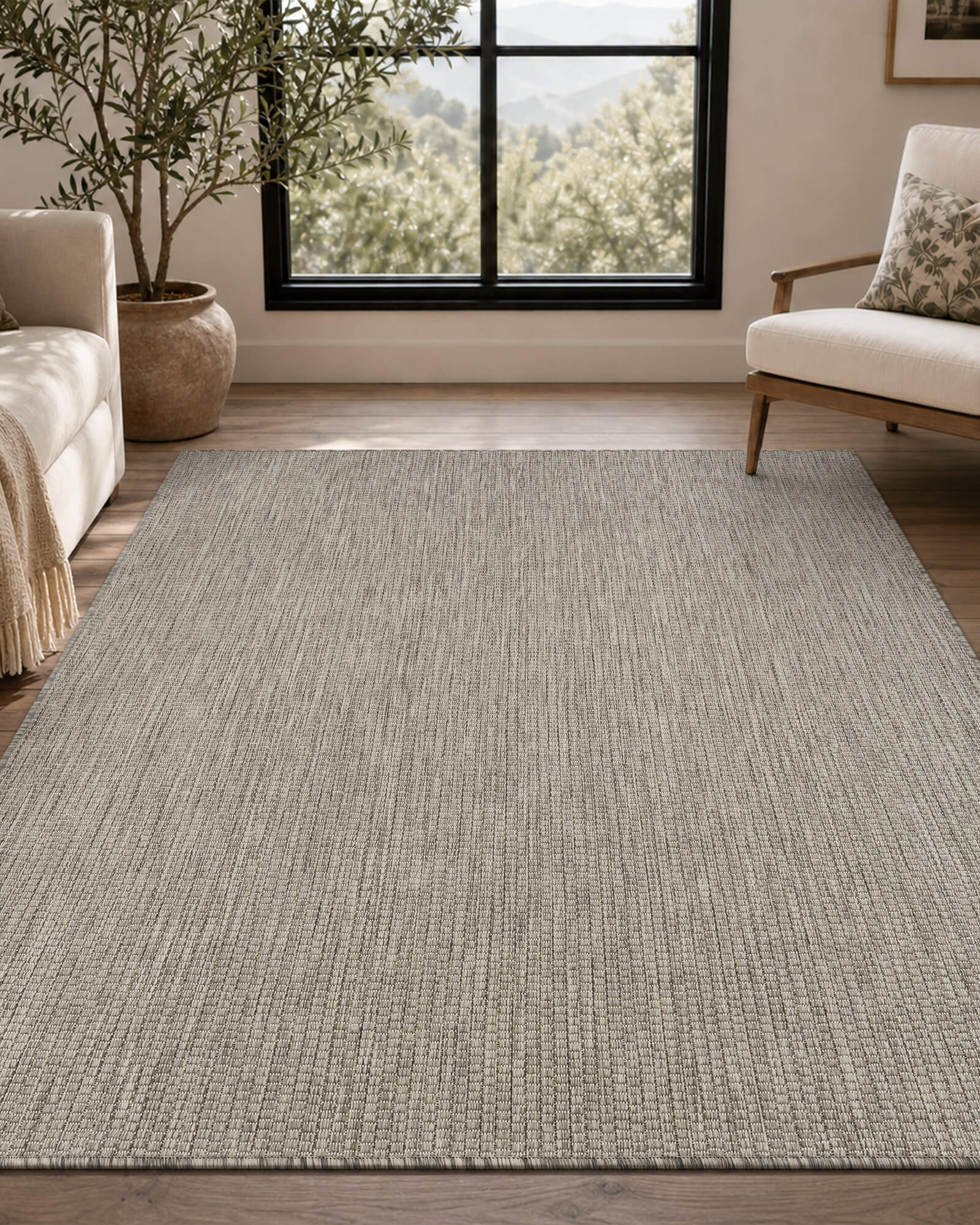 A light gray plain weave indoor outdoor area rug adds clean natural texture to a bright living room with neutral seating, wood floors, large windows, and a peaceful mountain view.