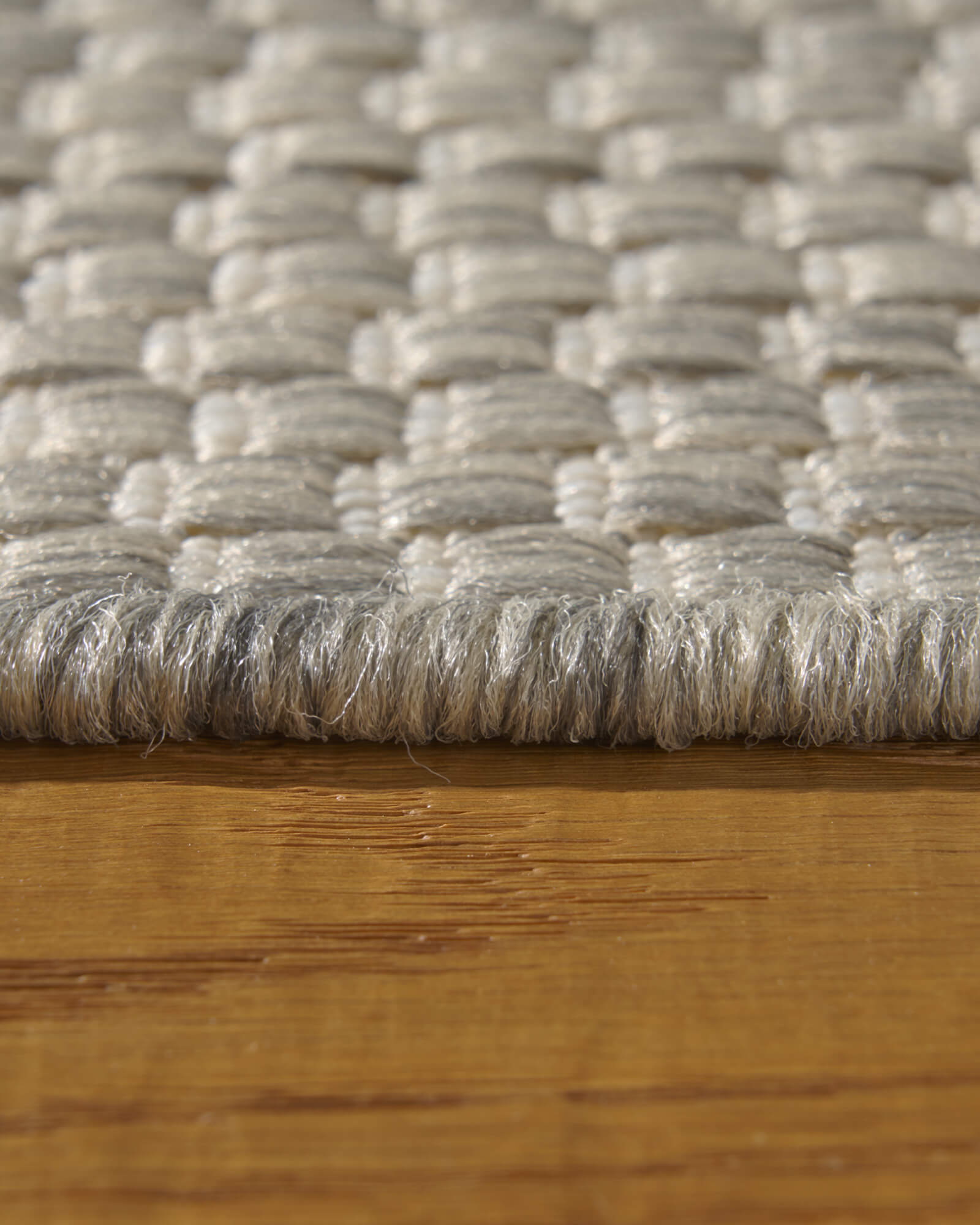 A macro close-up of a light gray plain weave outdoor rug shows its chunky woven threads, low edge profile, and durable textured surface for patios, decks, porches, and outdoor living areas.