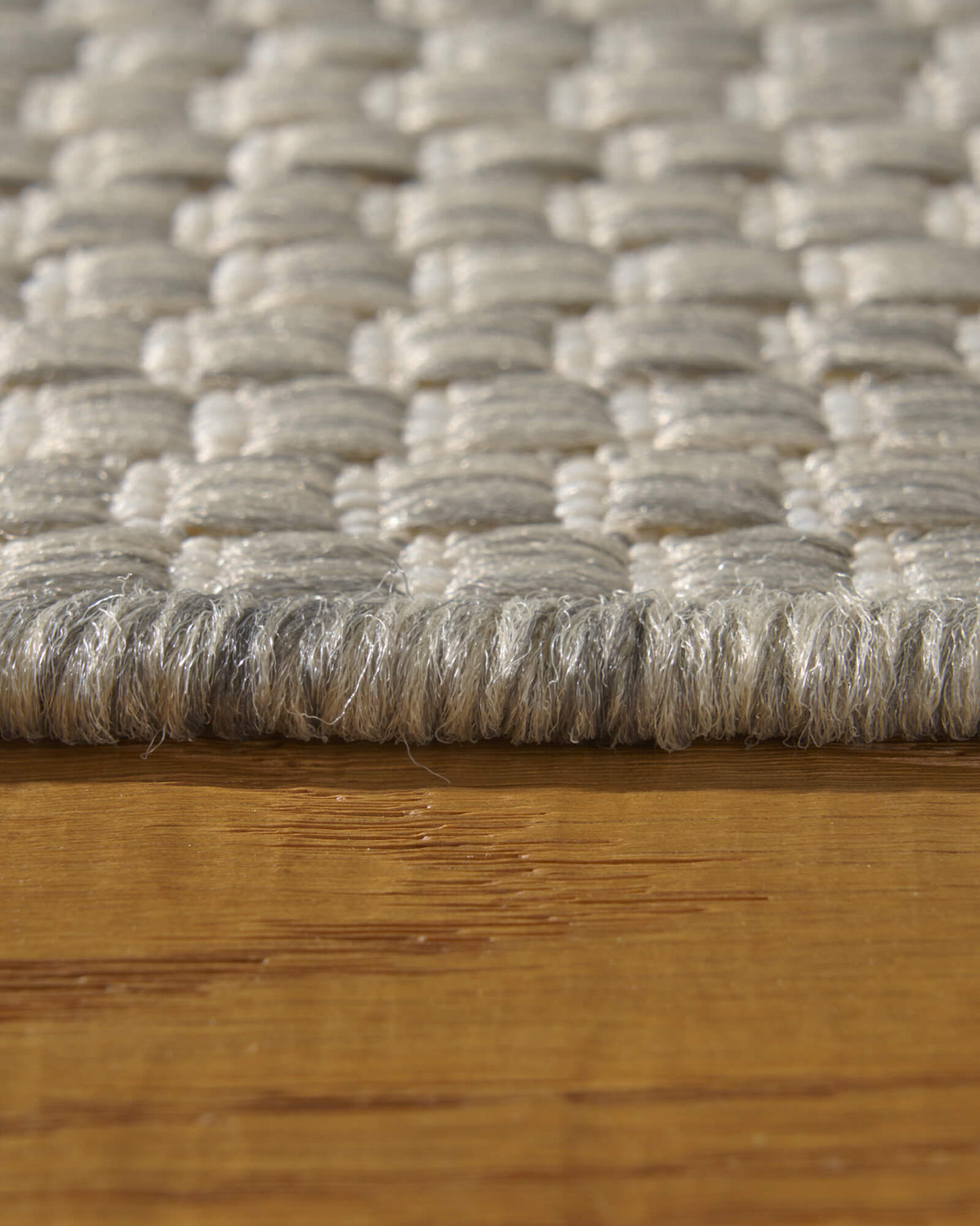 A macro close-up of a light gray plain weave outdoor rug shows its chunky woven threads, low edge profile, and durable textured surface for patios, decks, porches, and outdoor living areas.