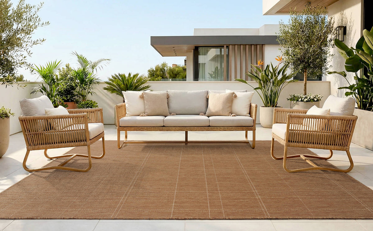 A light gray plain weave outdoor rug with subtle check line texture creates a clean modern patio seating area with woven chairs, a neutral sofa, tropical greenery, and weather-resistant outdoor style.