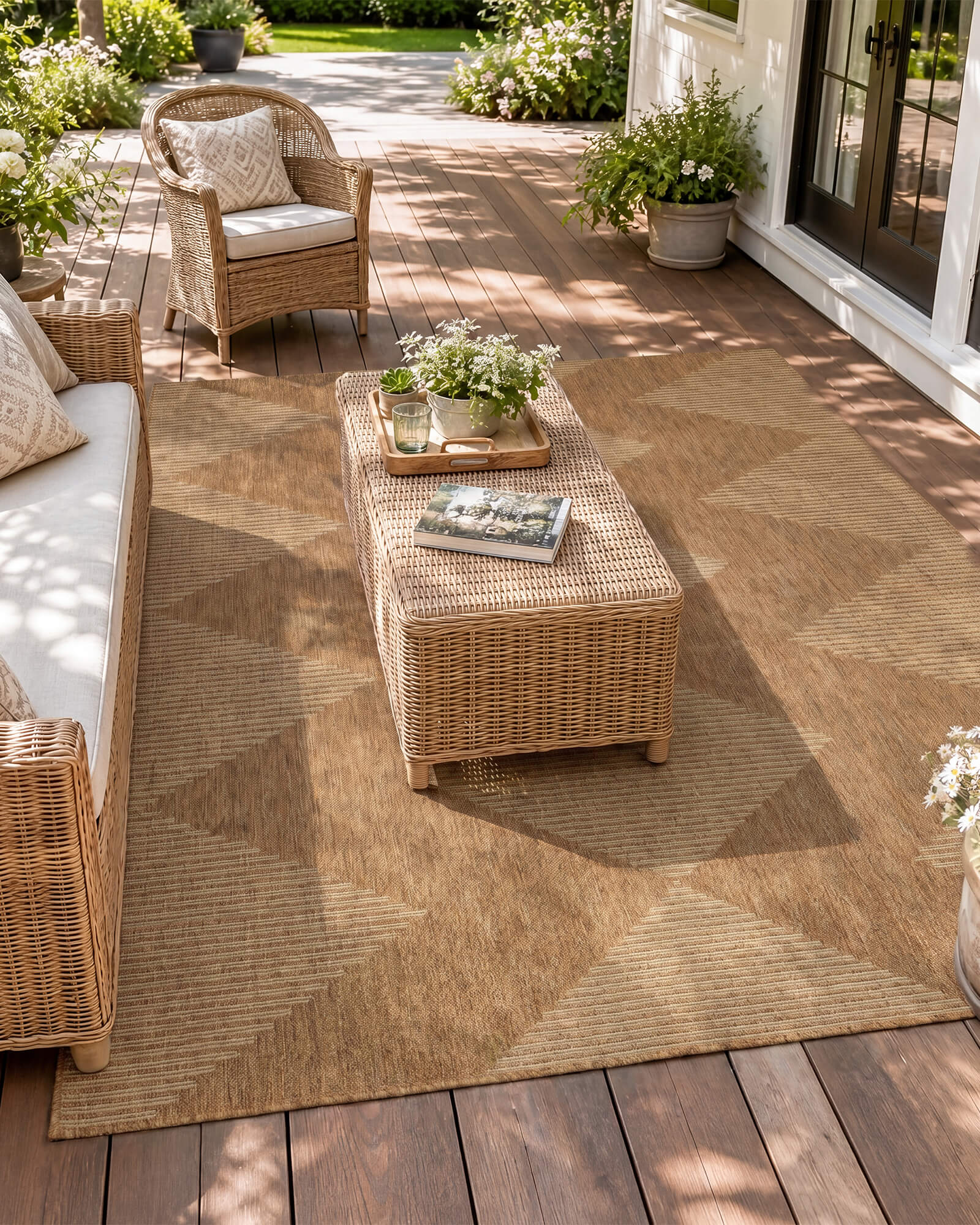 A natural woven indoor outdoor rug adds durable jute-look texture and easy-care style to a sunny patio seating area with wicker furniture, garden plants, and warm outdoor living decor.