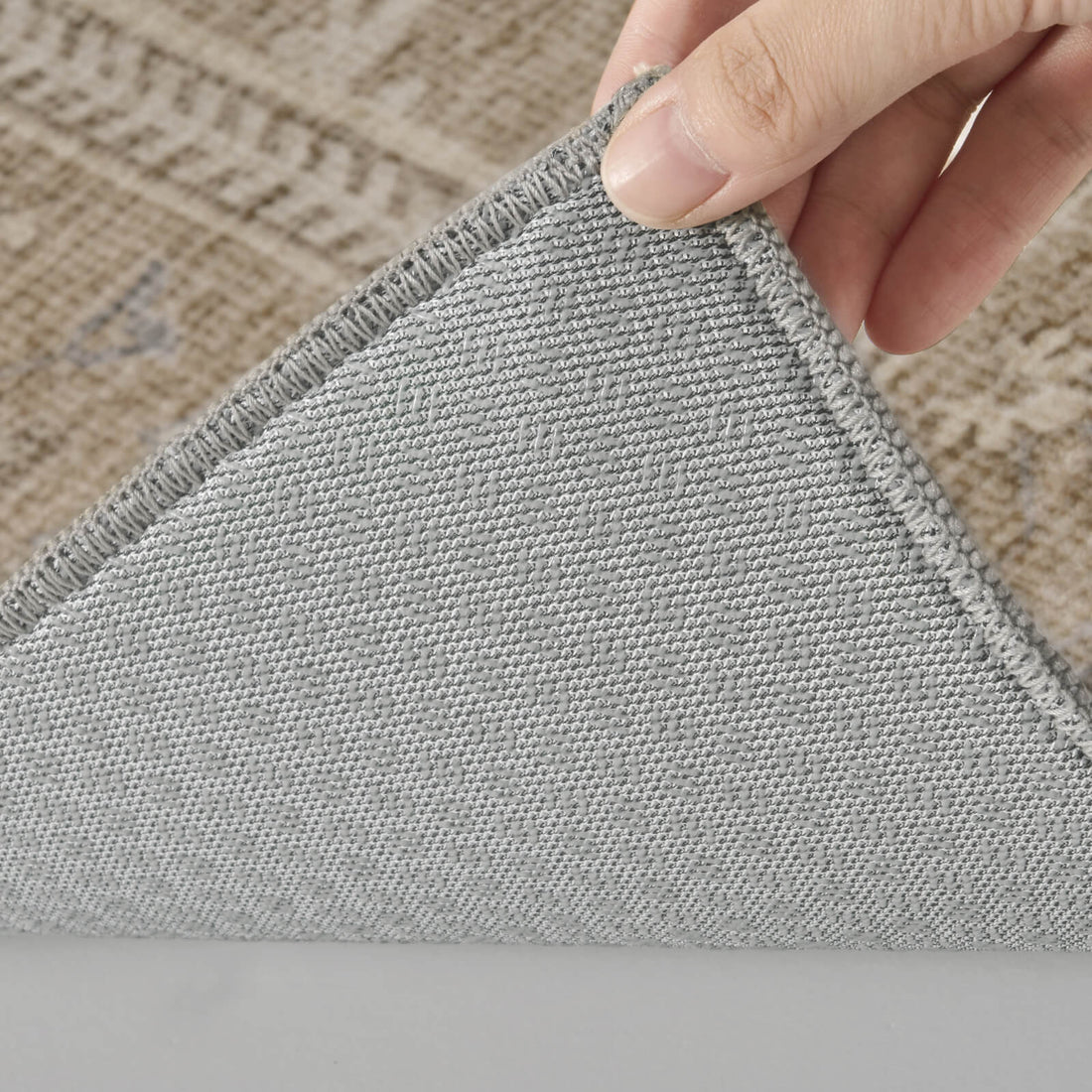 A close-up view of a neutral vintage washable area rug showing its gray grip backing, reinforced stitched edge, and flexible low-pile construction for stable everyday use in bedrooms, living rooms, and busy homes.