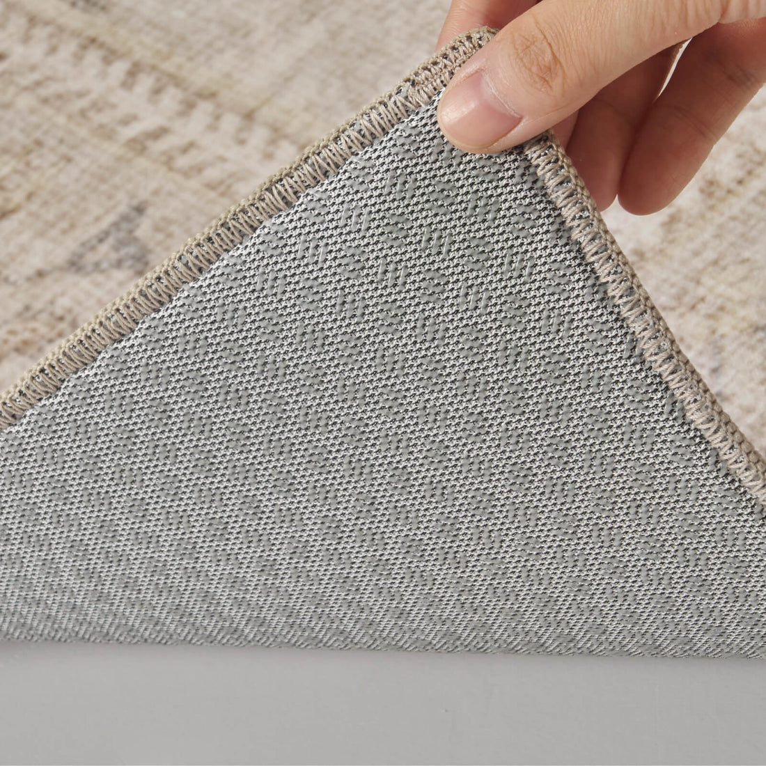 A close-up view of a neutral vintage washable rug showing its gray textured backing, stitched edge, and flexible corner construction for stable everyday use in living rooms, bedrooms, and busy family homes.