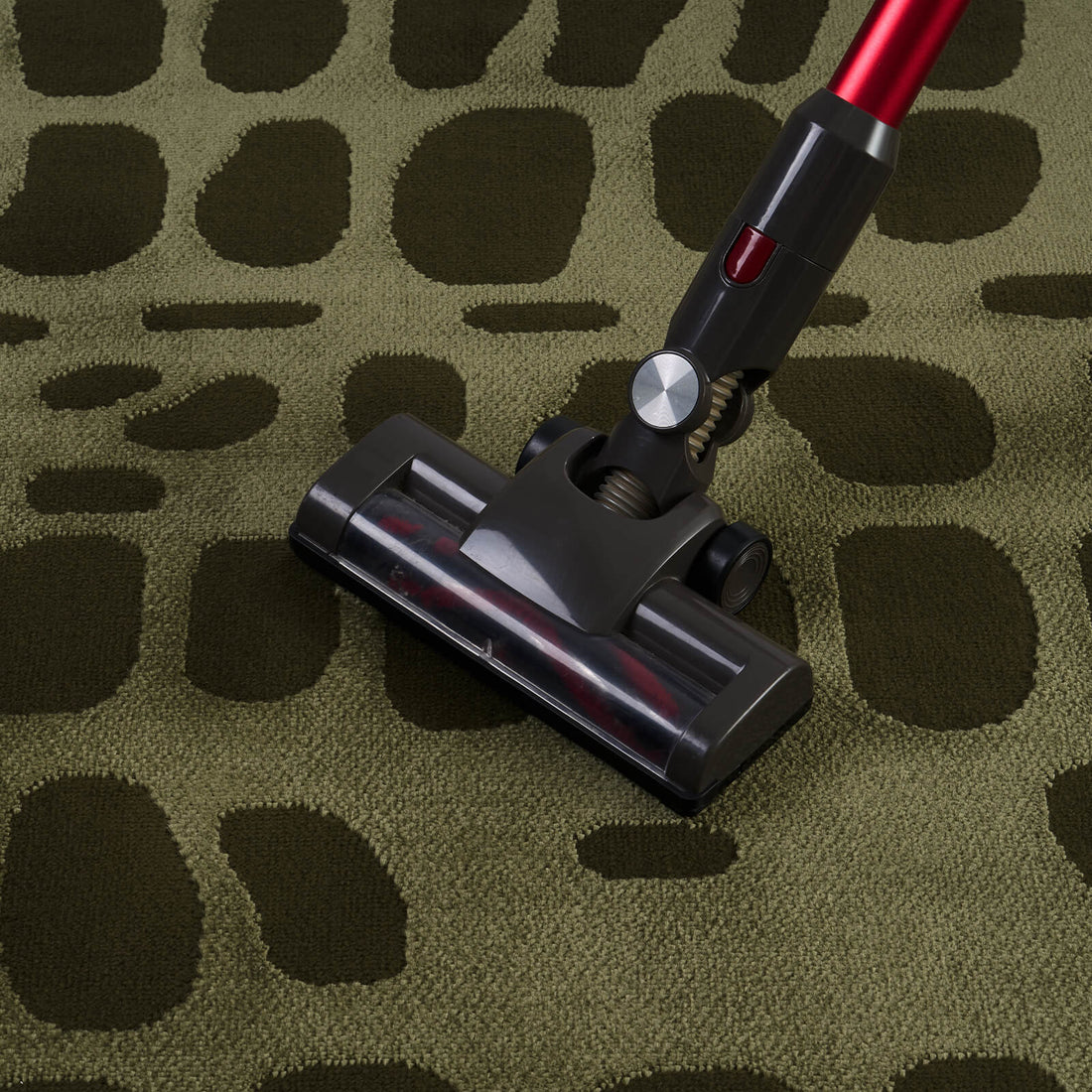 An olive green premium Wilton jacquard area rug is shown being vacuumed, highlighting its raised geometric texture, refined woven surface, and elevated easy-care design for high-end living rooms and designer-inspired homes.