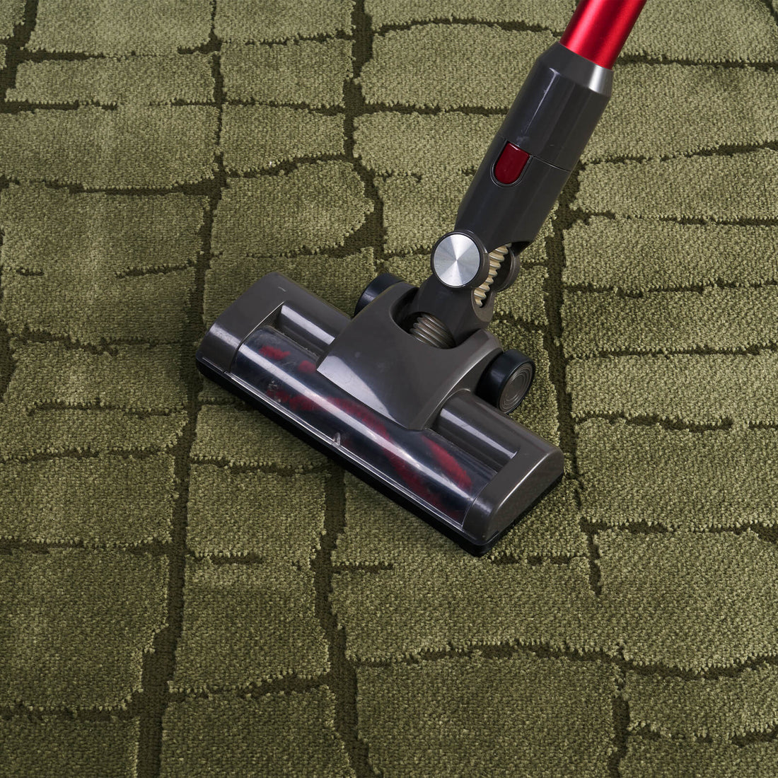 An olive green premium Wilton jacquard area rug is shown being vacuumed, highlighting its raised grid texture, dimensional woven surface, and refined easy-care finish for luxury living rooms and designer-inspired homes.