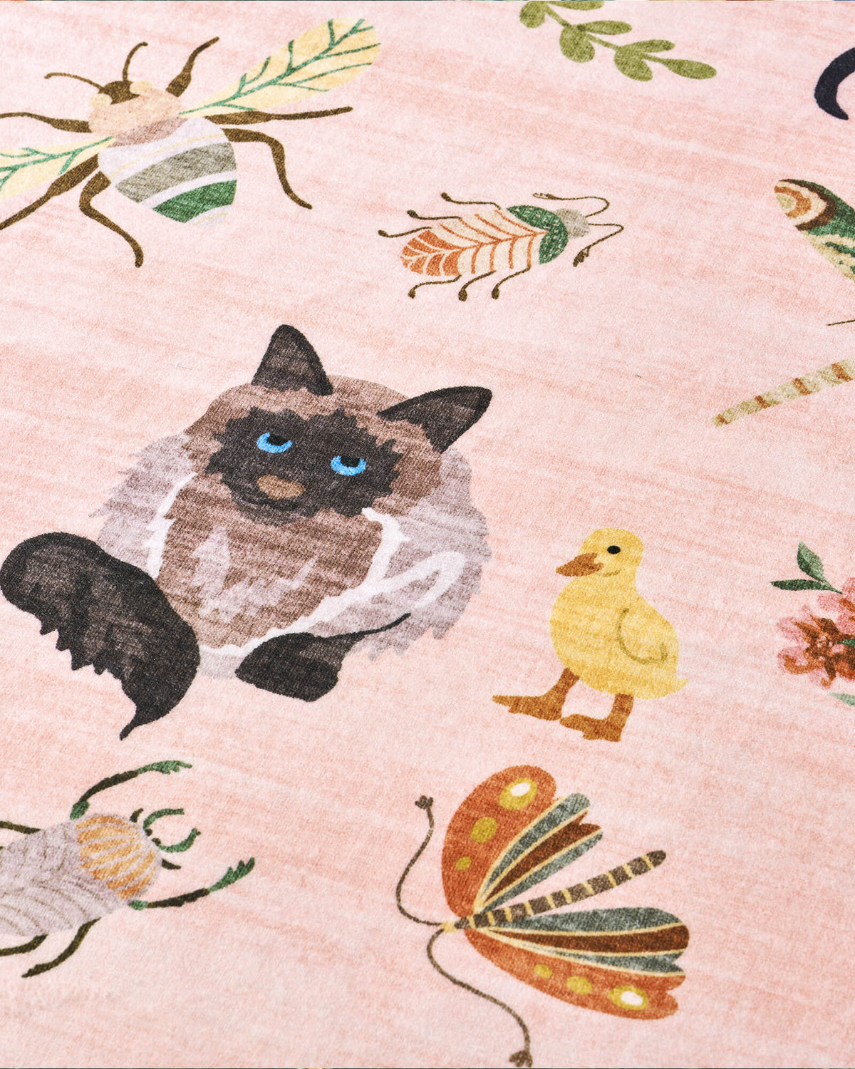 A close-up view of a pink soft kids rug highlights its cute cat, duck, butterfly, and bug illustrations, offering a gentle comfortable surface and playful charm for nurseries, playrooms, and children’s bedrooms.