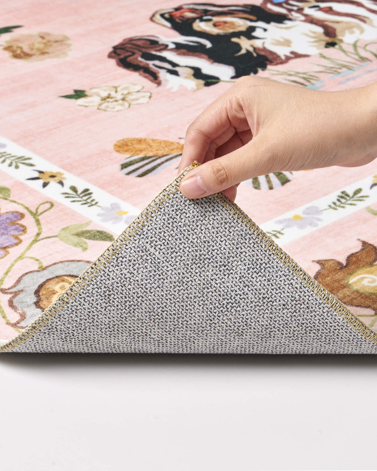 A close-up view of a pink soft kids rug showing its folded corner, gray non-slip backing, cute animal border pattern, and neatly finished edge for safe, cozy nursery, playroom, and children’s bedroom use.
