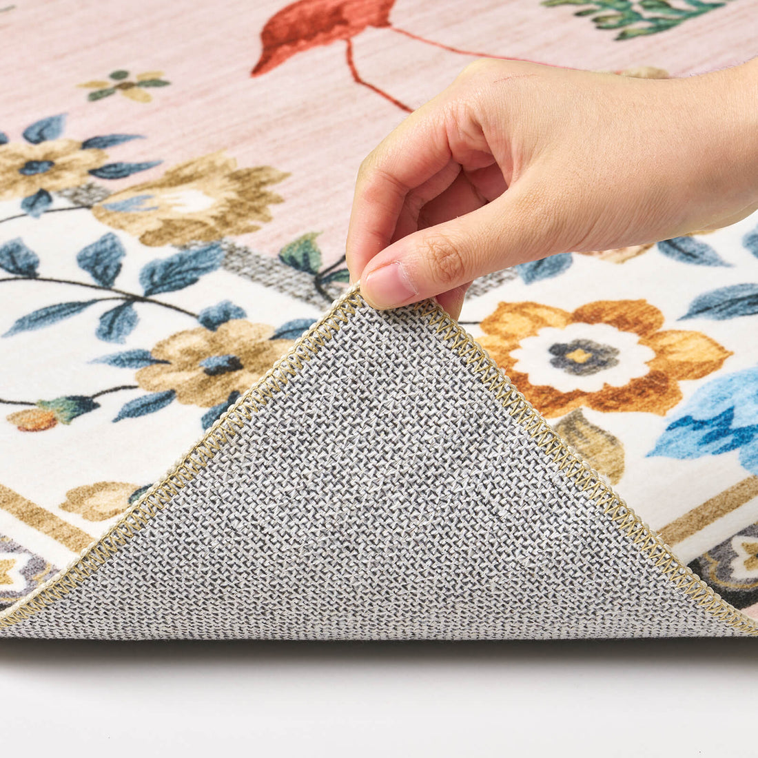 A close-up view of a pink soft kids rug showing its folded corner, gray non-slip backing, floral border pattern, and neatly finished edge for safe, cozy nursery, playroom, and children’s bedroom use.