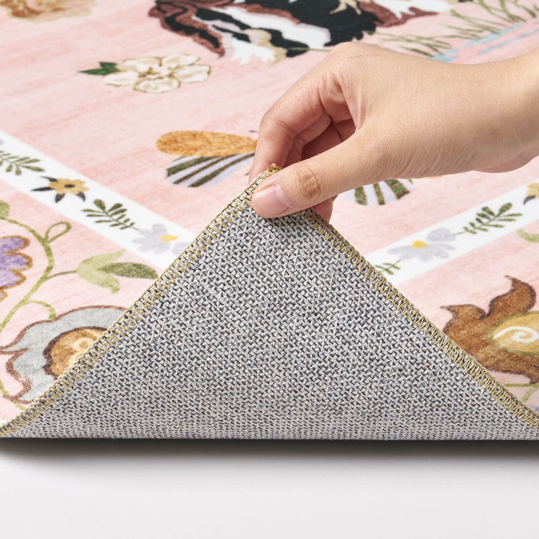 A close-up view of a pink soft kids rug showing its folded corner, non-slip backing, neatly bound edge, and cute animal floral pattern for safe, cozy playroom and nursery use.