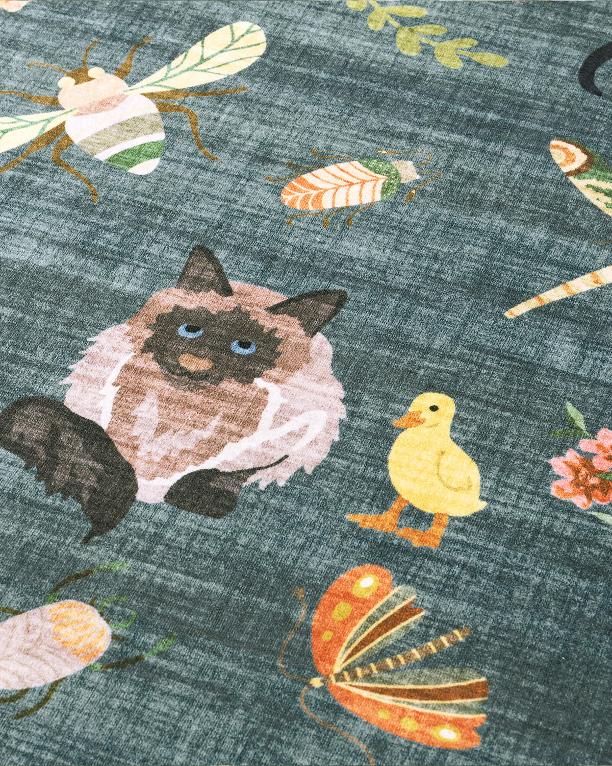 A close-up view of a teal soft kids rug highlights its cute cat, duck, butterfly, and bug illustrations, offering a gentle comfortable surface and playful charm for nurseries, playrooms, and children’s bedrooms.