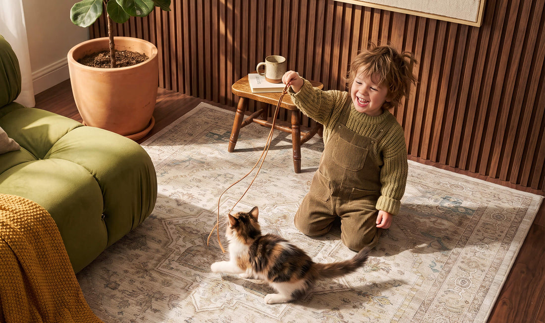 A vintage washable area rug with a softly distressed Persian-inspired pattern creates a cozy, kid- and pet-friendly play space where a young child enjoys playing with a kitten. Its soft, comfortable surface and timeless design complement a warm living room with an olive green sofa, wood accents, and natural sunlight.