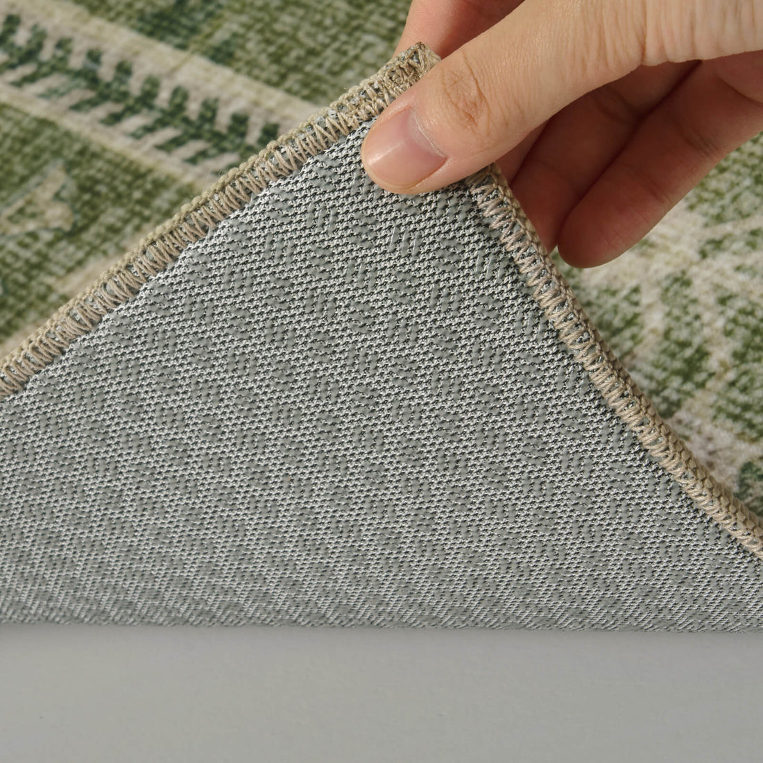 A close-up view of a washable green vintage floral area rug showing its durable non-slip backing, reinforced stitched edge, and soft low-pile construction for everyday comfort and stability in busy homes.
