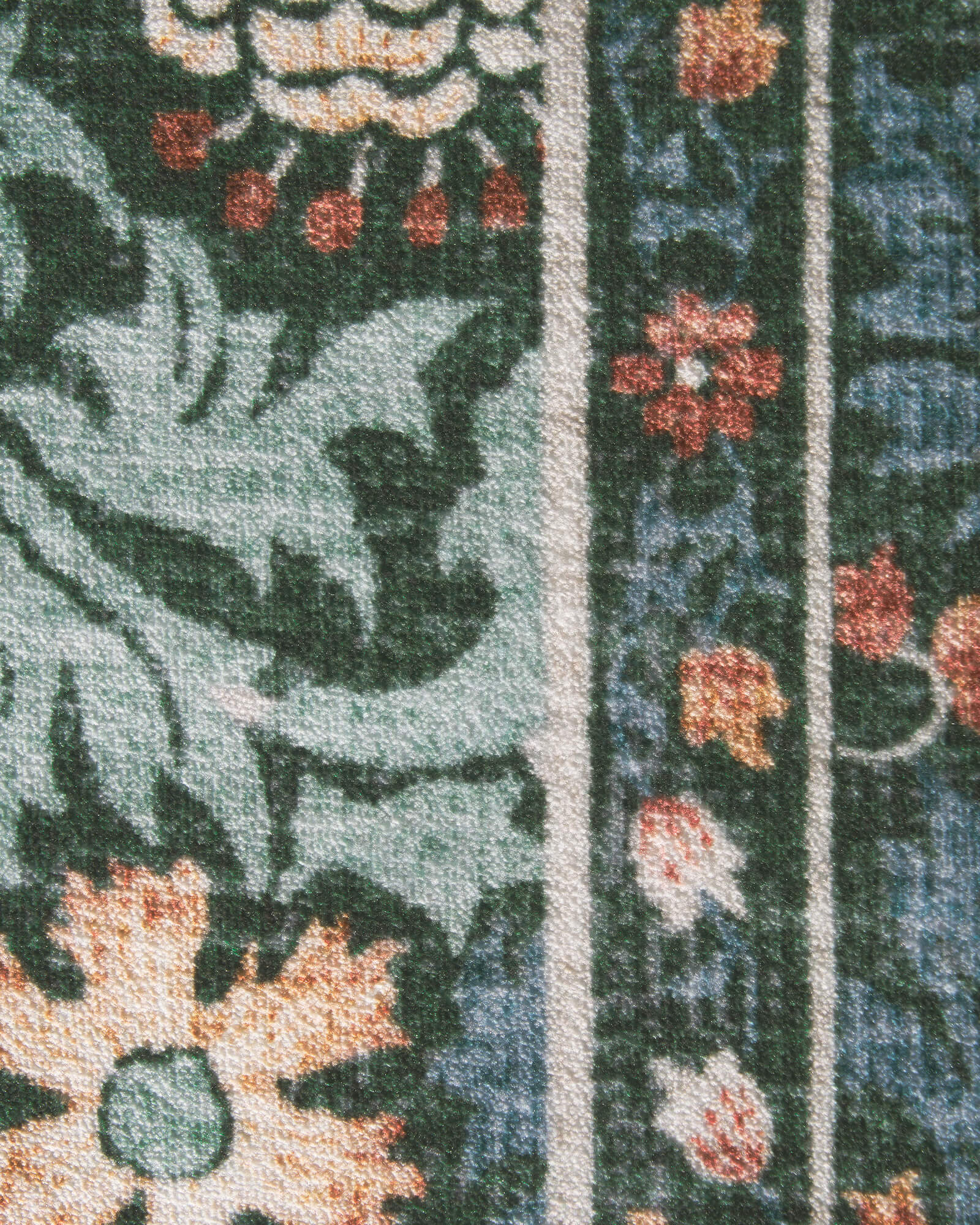 A close-up view of a washable vintage floral area rug featuring a dark green botanical pattern, colorful floral details, and a soft textured surface designed for cozy traditional home interiors.