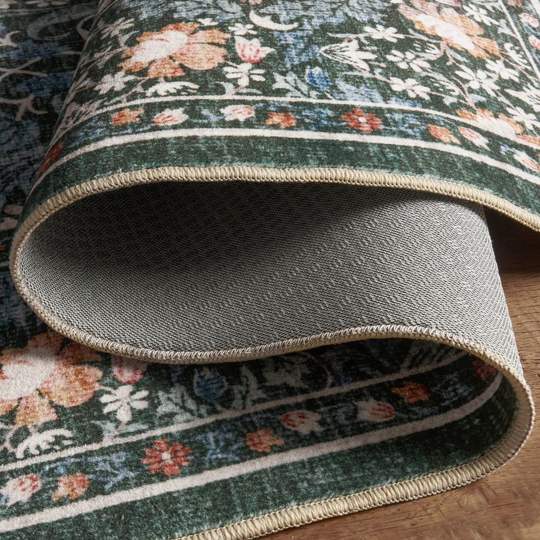 A close-up view of a washable vintage floral area rug featuring a dark green botanical pattern, soft low-pile texture, finished edges, and durable non-slip backing for comfortable everyday home use.